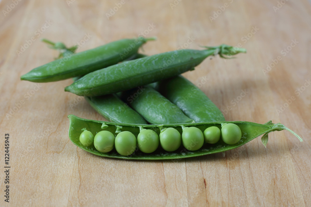 Pods of green peas on wooden cutting board close up Pods of green peas on wooden cutting board close up
