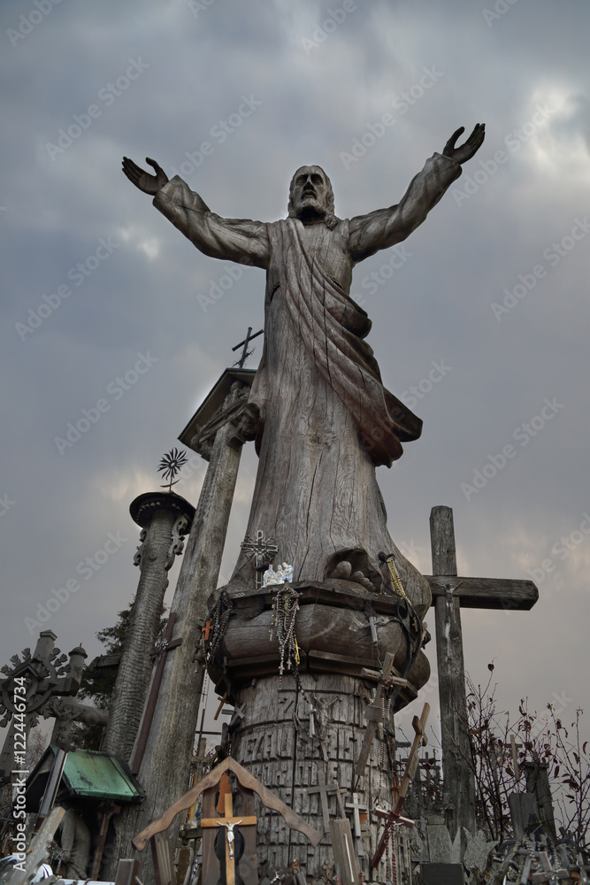 Fototapeta premium Catholicism religion landmark - The Hill of Crosses in Lithuania - Statue of saint under dark cloudy sky