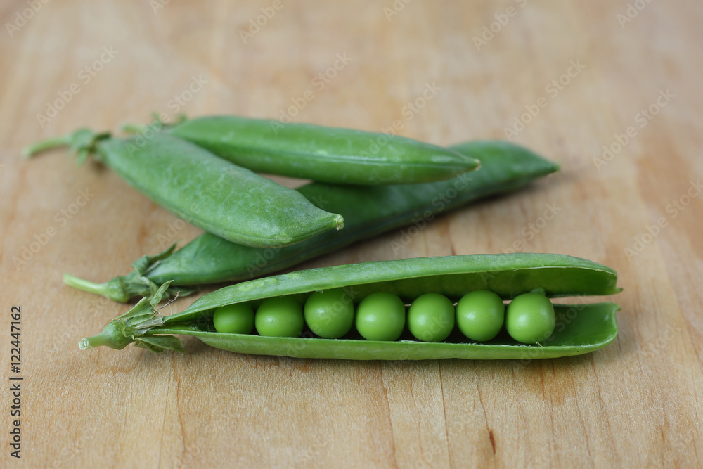 Pods of green peas on wooden cutting board close up Pods of green peas on wooden cutting board close up