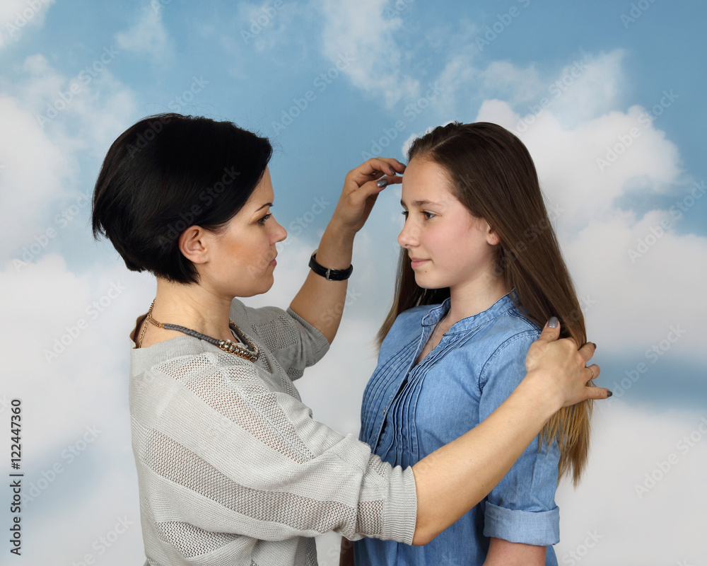 Mother corrects daughter hairstyle on cloudy blue sky background - Family relations and parenting concept Mother corrects daughter hairstyle on cloudy blue sky background - Family relations and parenting concept