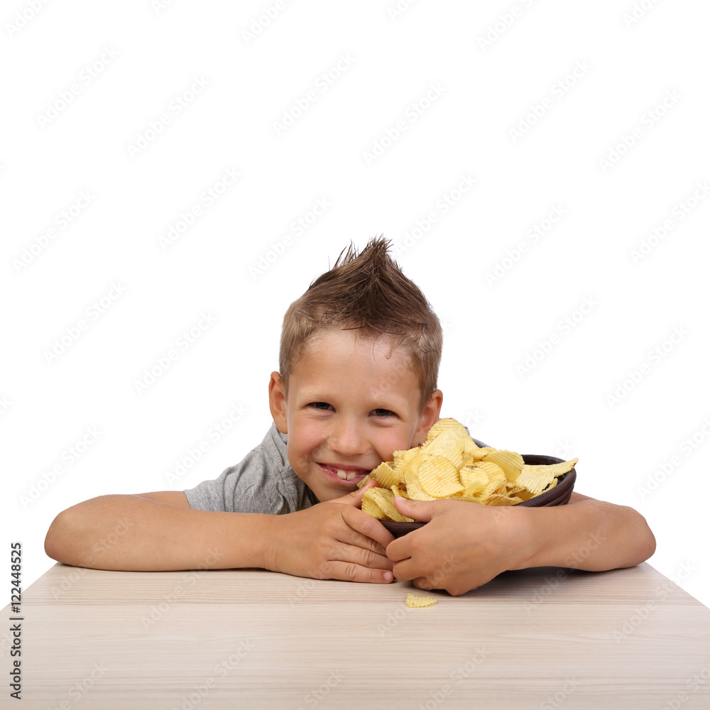 Happy teenage boy sits at the table embracing bowl with potato chips isolated on white background in square Happy teenage boy sits at the table embracing bowl with potato chips isolated on white background in square
