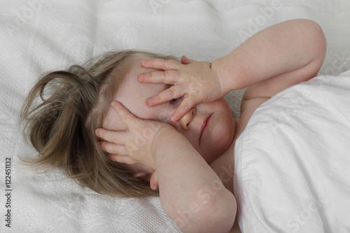 Wish to sleep - Infant baby in bed under blanket closes her eyes with hands