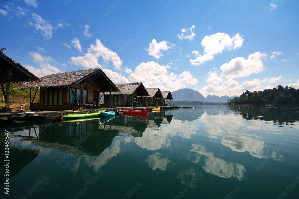Naklejka premium Beautiful scenery of houseboat and the beautiful water reflection with clear sky at lake river in natural attractions,Ratchaprapha Dam at Khao Sok National Park,Surat Thani Province in Thailand.