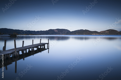 Fototapeta Naklejka Na Ścianę i Meble -  Wooden pier or jetty on a blue lake sunset and sky reflection on