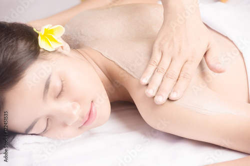 Young woman receiving back mask cream at spa center