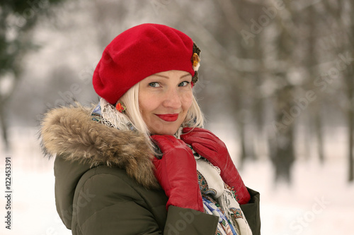 Mature woman in red beret and winter clothes on blur natural snowy background - with warming photo filter