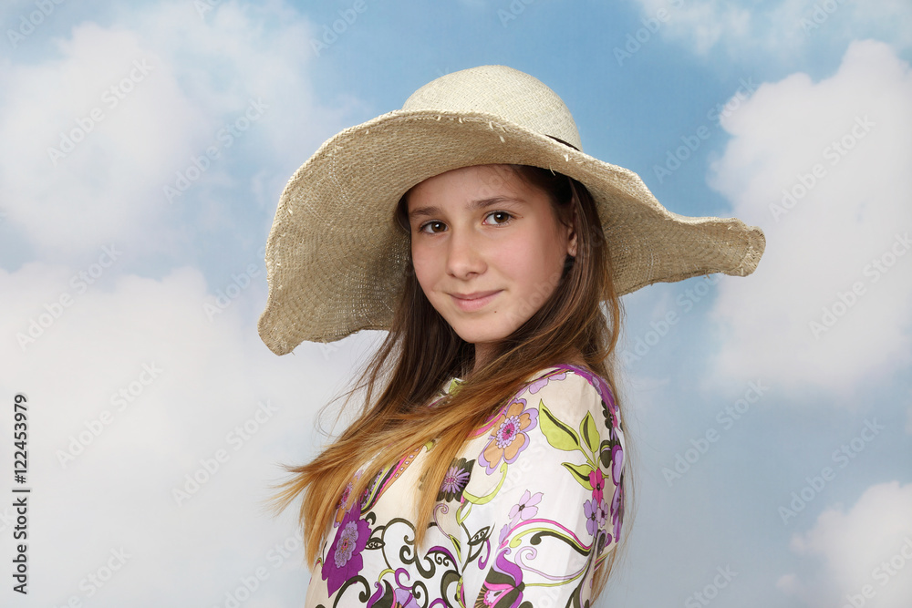 Long haired teenage girl in big hat on cloudy blue sky background - travel and vacation concept
