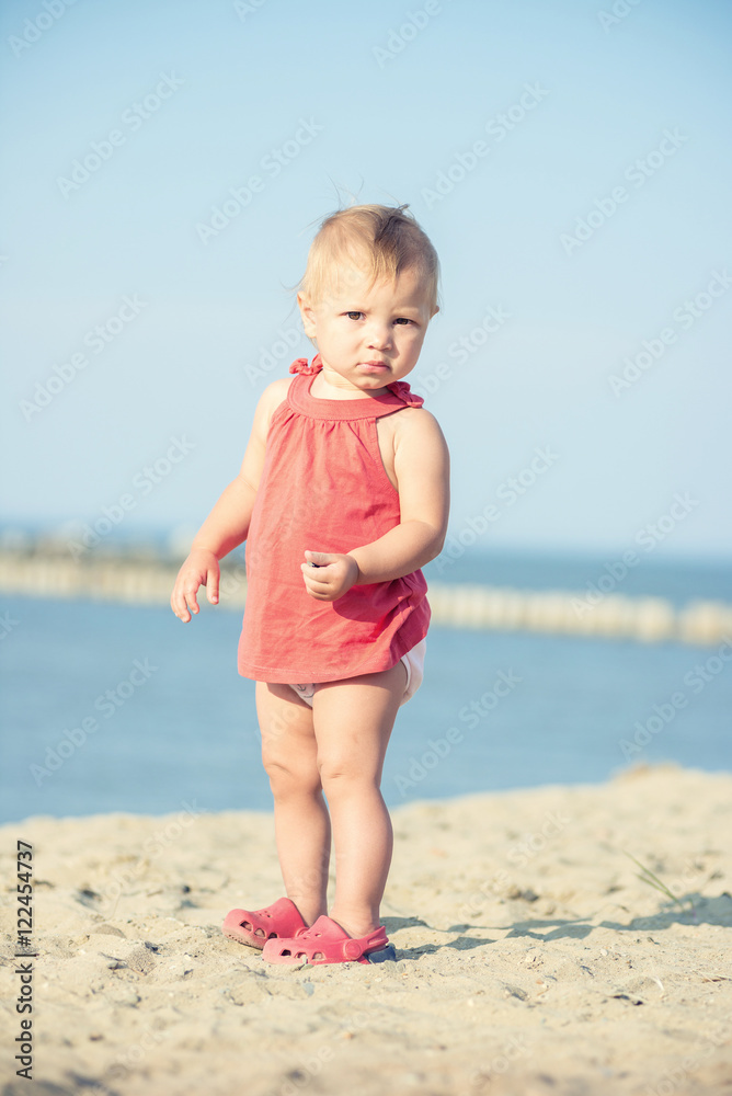 Baby playing on the sandy beach near the sea. Cute little girl in red dress with sand on tropical beach. Ocean coast. Baby playing on the sandy beach near the sea. Cute little girl in red dress with sand on tropical beach. Ocean coast.