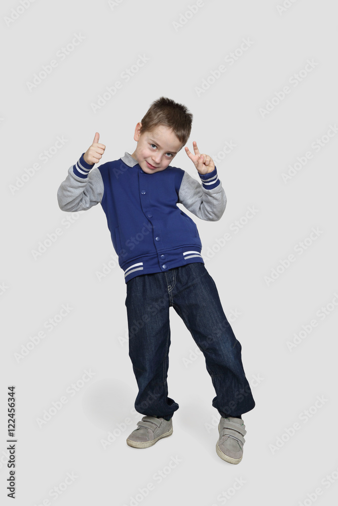 Happy little boy in casual clothes demonstrates that all is good posing on gray background Happy little boy in casual clothes demonstrates that all is good posing on gray background