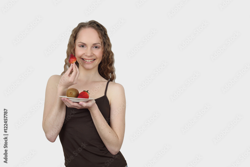 Pretty young woman in shirt with bare arms eats red strawberry on gray background with copy space for advertising text - Beauty, health and diet concept Pretty young woman in shirt with bare arms eats red strawberry on gray background with copy space for advertising text - Beauty, health and diet concept