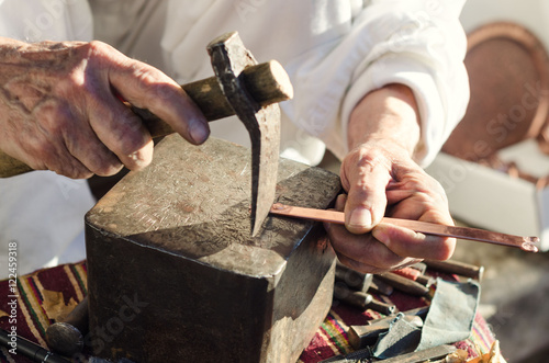 Old craftsman working with hammer on cooper bangle