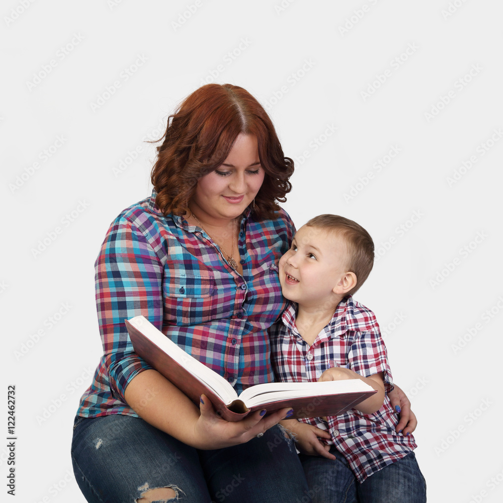 Red haired woman sits together with little boy reading a big book - Mother and little son on gray background in square - Education inside family Red haired woman sits together with little boy reading a big book - Mother and little son on gray background in square - Education inside family