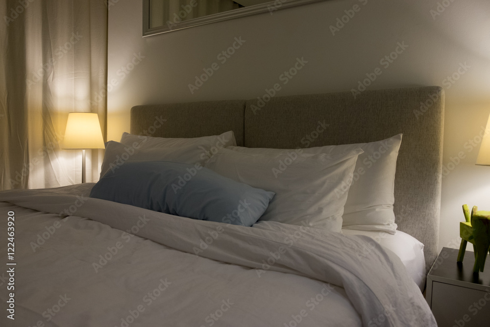 stylish bedroom interior design with cream patterned pillows on bed and decorative table lamp.