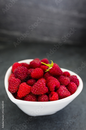 Fresh raspberries in bowl on dark stone background. Space for text.