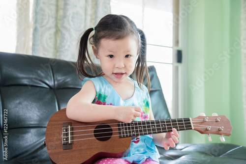 Little asian girl playing ukulele at home