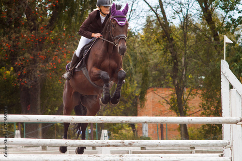 Young rider girl jumping over barier on her course © skumer