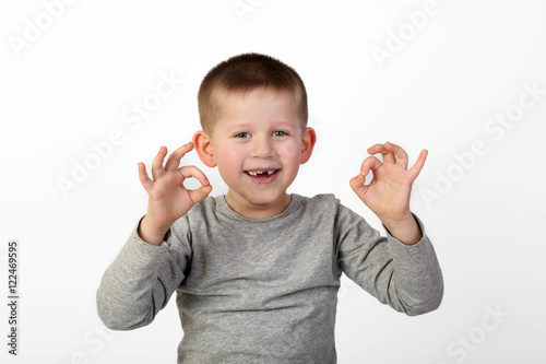 Little toothless boy with wide happy smile on face shows okey sign on gray background