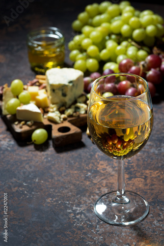 cheeseboard, fruit and glass of white wine on a dark background