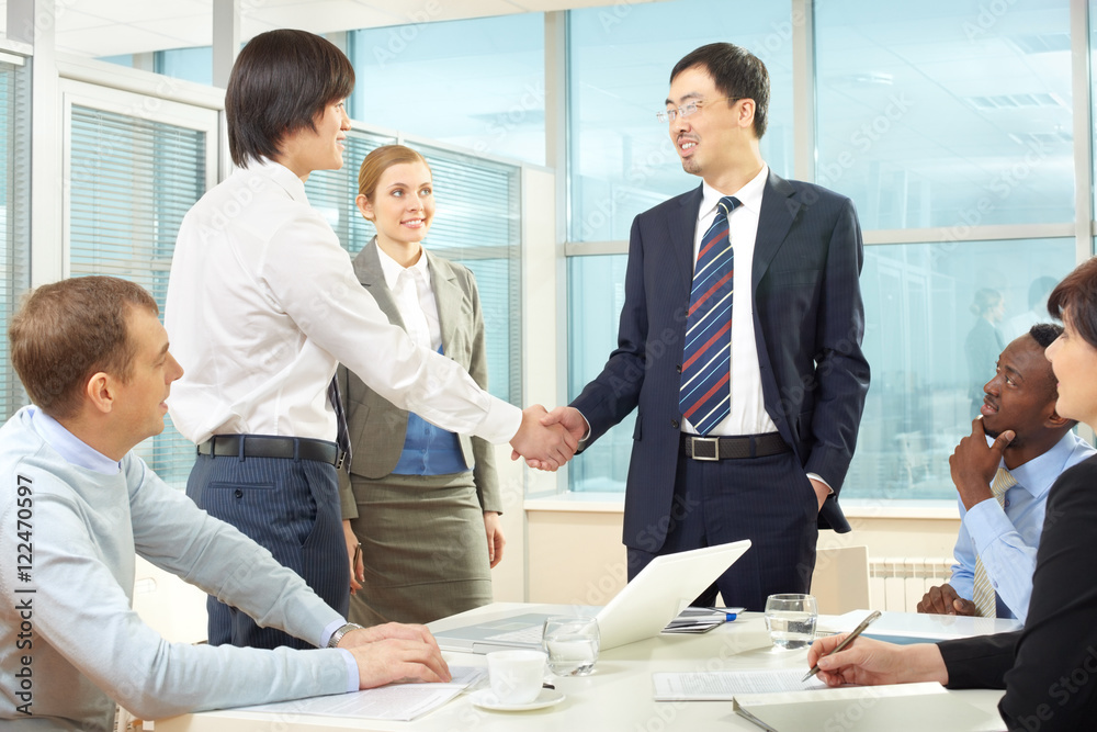 Businessmen handshaking while business people sitting at the table Businessmen handshaking while business people sitting at the table