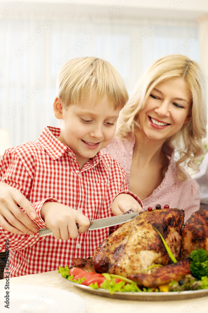 Little boy cutting turkey together with his mother at Thanksgiving Day 