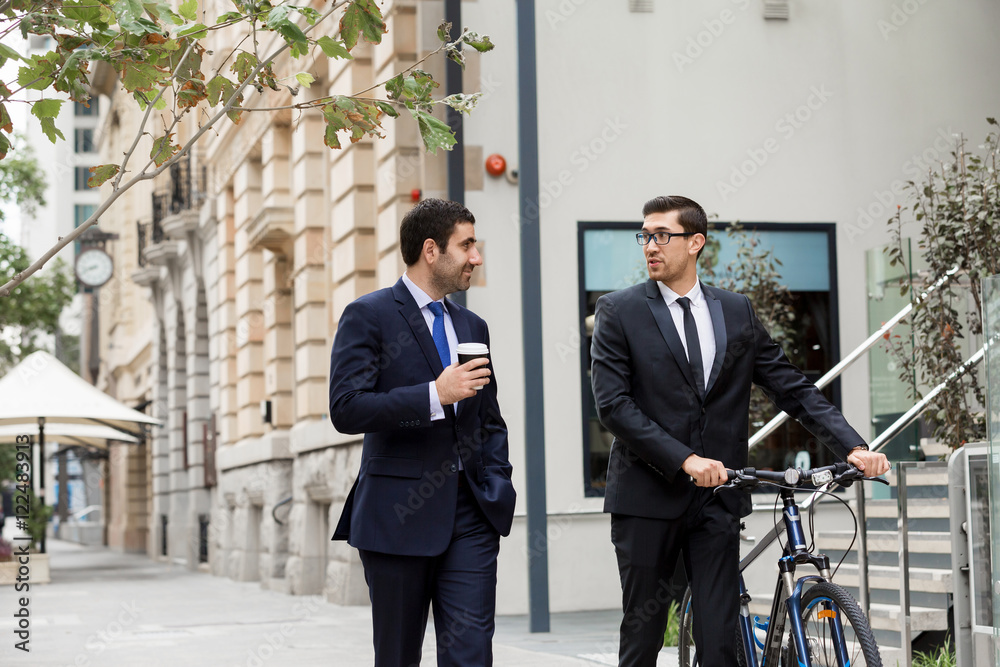 Two young businessmen with a bike in city centre