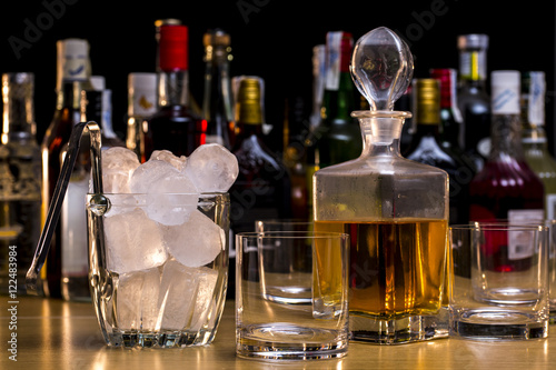 Whisky bottle beside a ice bucket and empty glasses in front of different liquors