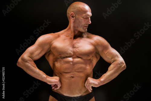 Sports training bald man bodybuilder shows muscles of the chest and press, studio dark background