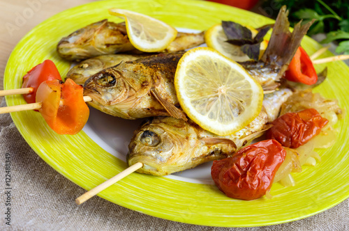 Fried fish (carp) on skewers with pieces bell pepper, sun-dried tomatoes and lemon. Close up