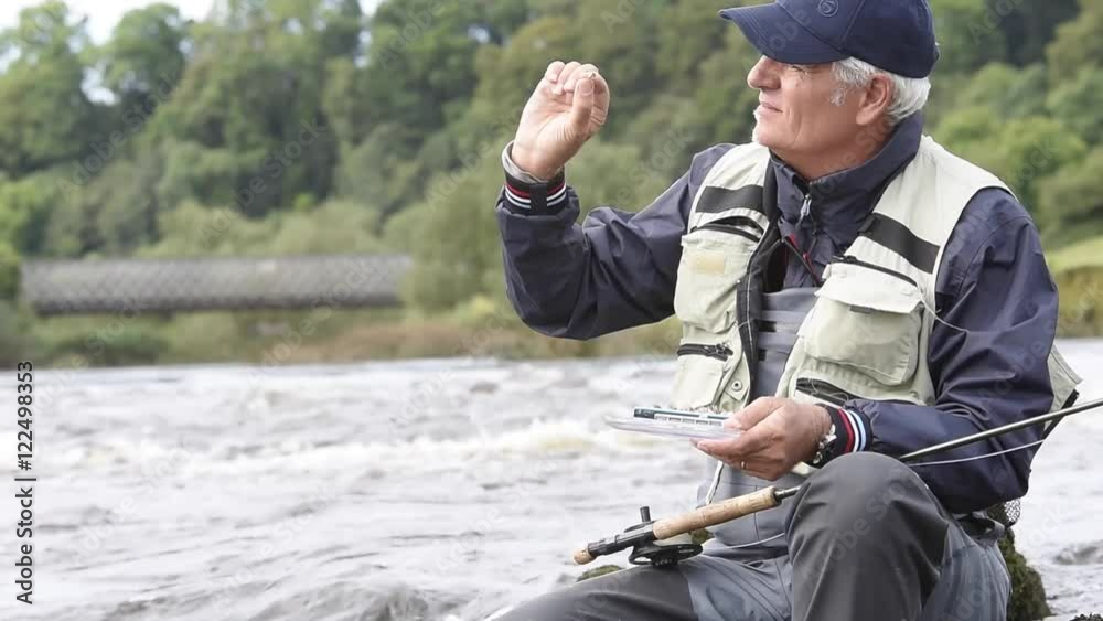 Fly-fisherman sitting on rock, choosing fly Fly-fisherman sitting on rock, choosing fly