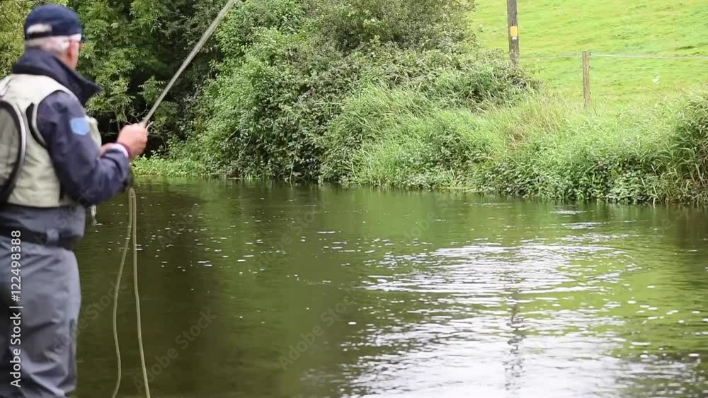 Fly-fisherman fishing from riverbank Fly-fisherman fishing from riverbank