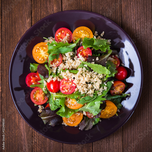 Fresh healthy salad with quinoa, cherry tomatoes and mixed greens (arugula, mesclun, mache) on wood background top view. Food and health. Superfood.