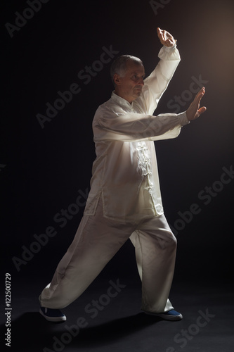 Quadro su tela Senior man enjoys exercise Tai Chi indoor.