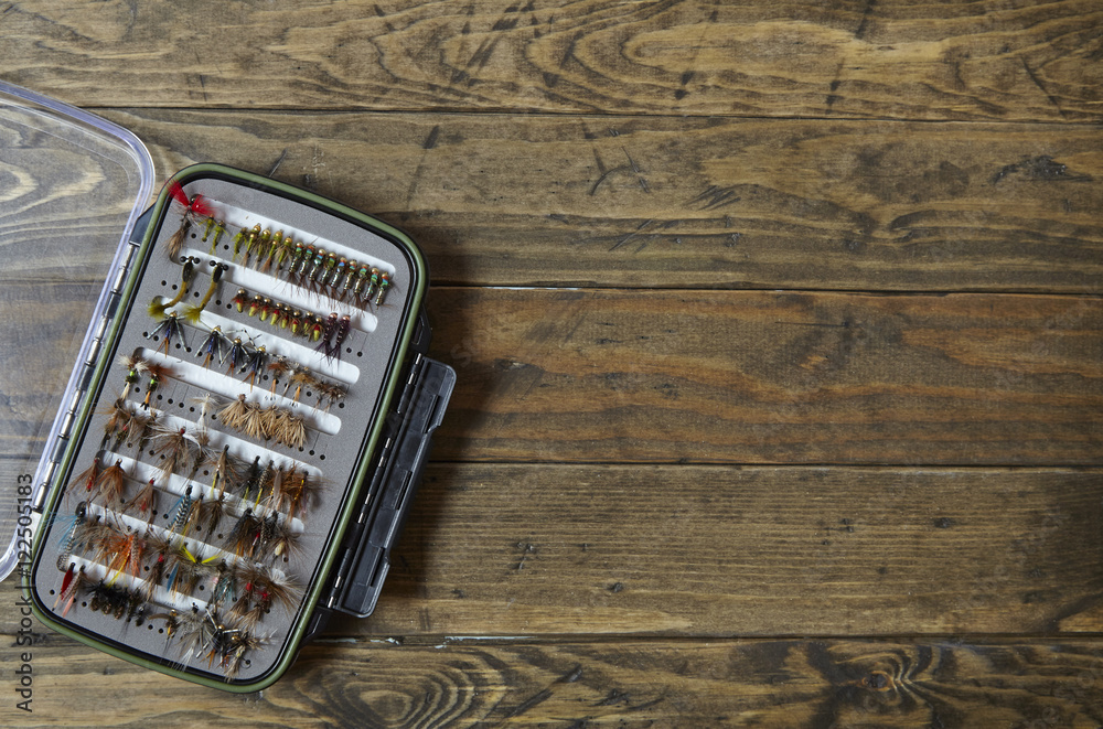 Fishing fly box arranged on a rustic wooden background to form a