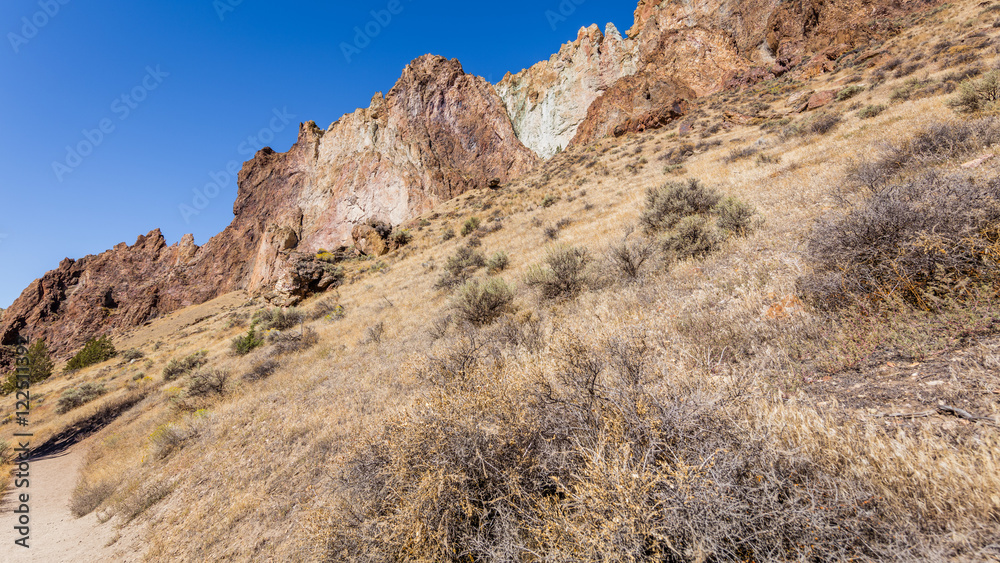 The path among the rocks. The sheer rock walls. Beautiful landscape of yellow sharp cliffs. Dry yellow grass grows on the slopes of the mountains. Smith Rock state park, Oregon