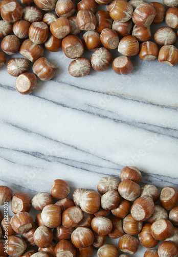 Whole hazelnuts arranged on a white marble background to form a page border