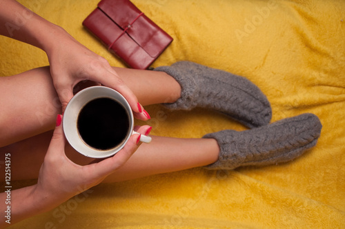 Woman in knitted socks on the sofa holding a cup of coffee