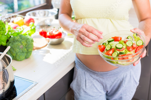 Schwangere Frau mit Babybauch isst gesunden Salat in Küche photo