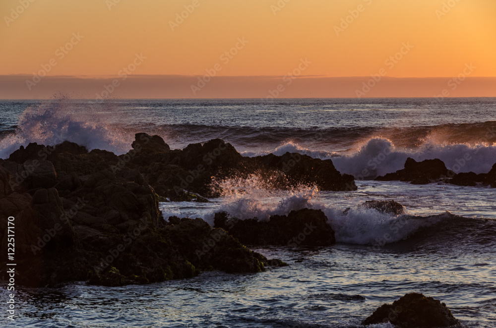 Multiple waves crashing on rocks at sunset