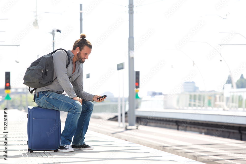 Cool guy sitting on suitcase waiting for train