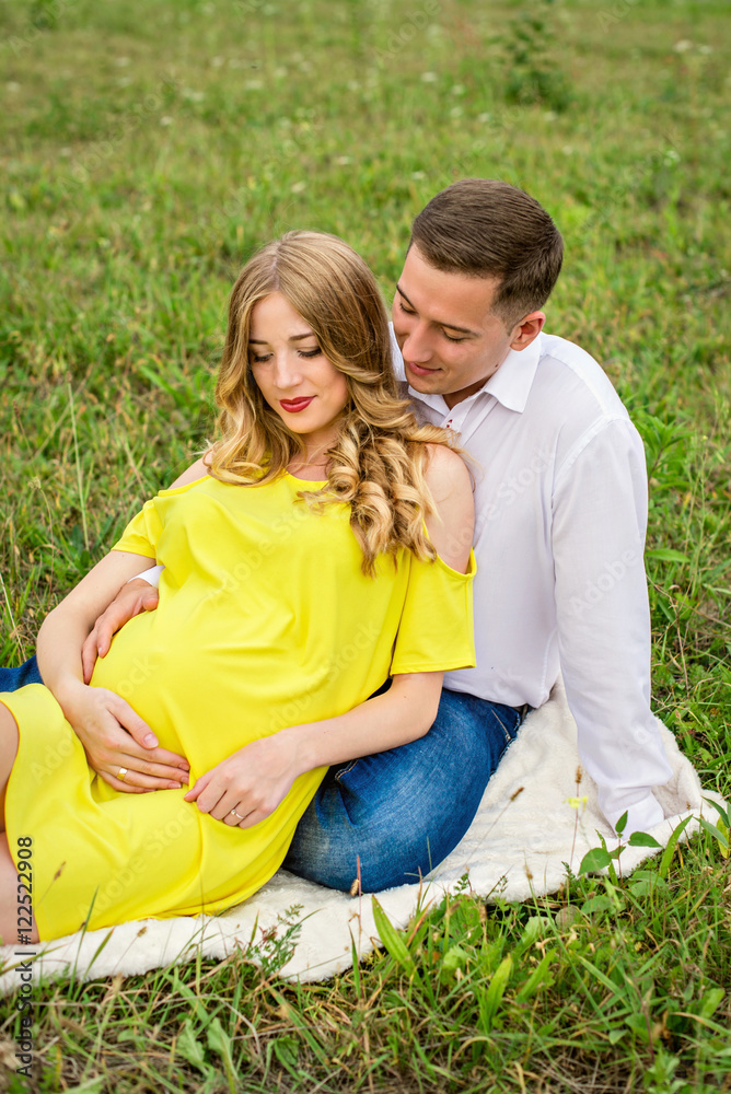 Fototapeta premium Portrait happy pregnant couple sitting on a blanket on grass