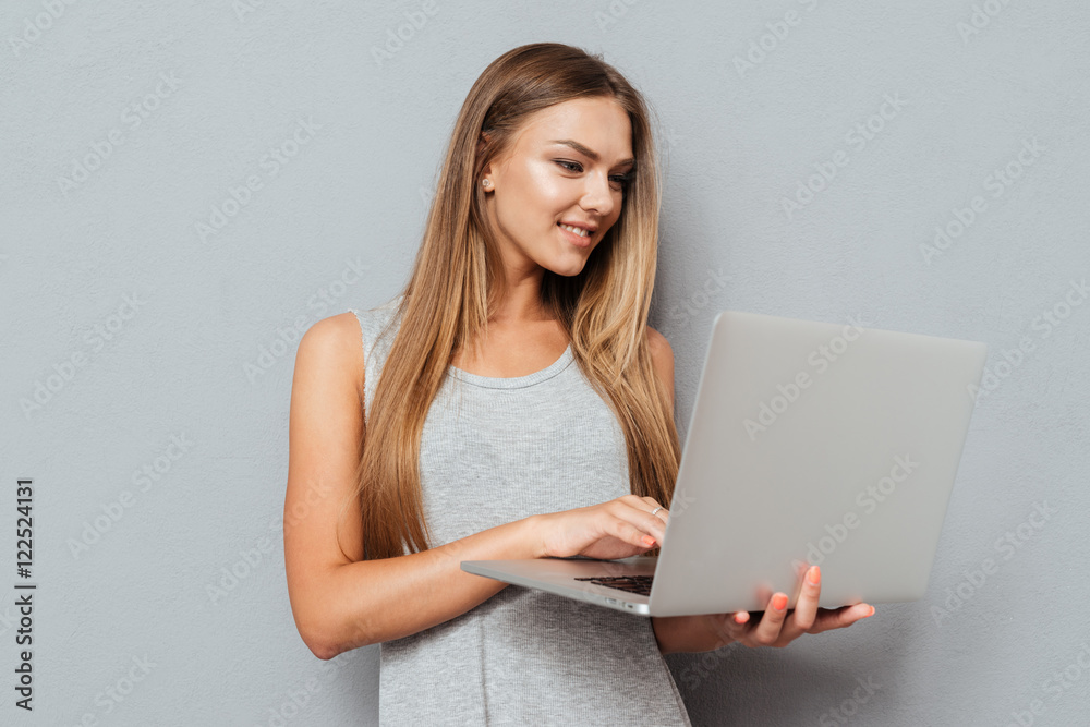 Smiling cute girl standing and using laptop Smiling cute girl standing and using laptop