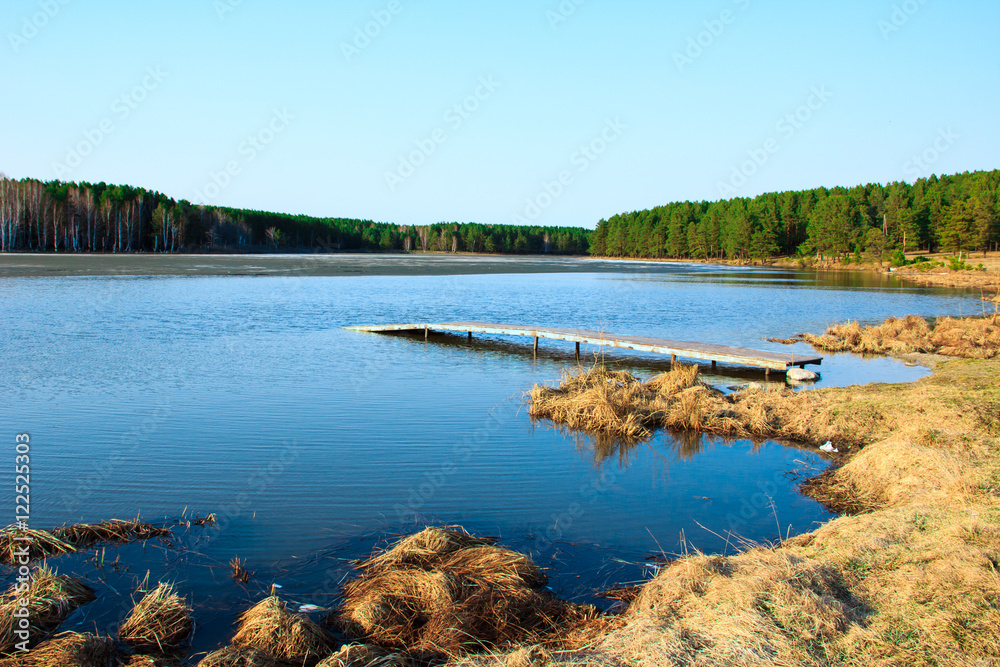 Landscape with a secluded lake, old pier, hay and pine forest around.