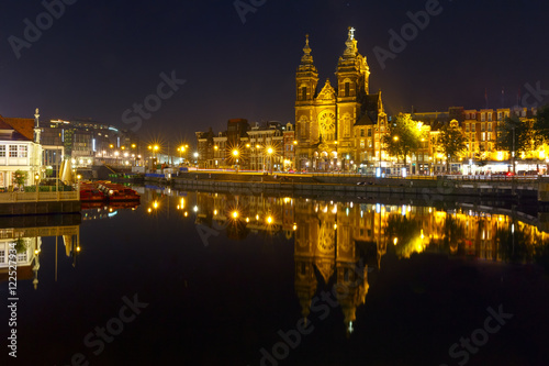 Night city view of Amsterdam canal with Basilica of Saint Nicholas and its mirror reflection in the water, Holland, Netherlands. Long exposure.