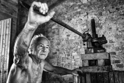 Foto Old shirtless winemaker farmer working on a traditional wine press