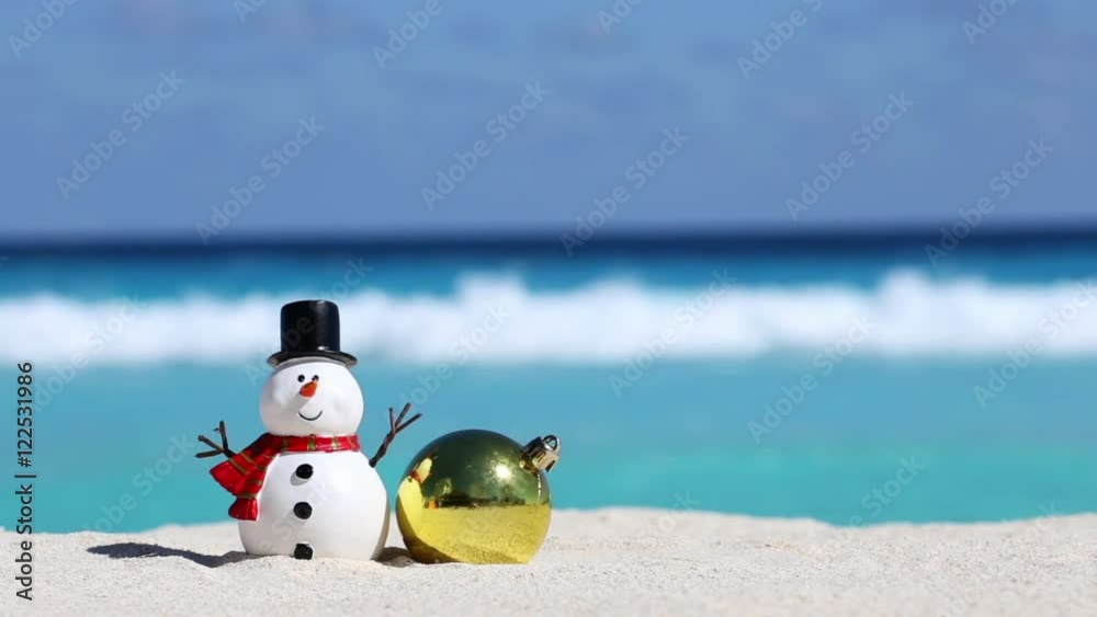 Snowman toy and christmas decoration ball at sandy beach on Caribbean sea background. New Year celebration
