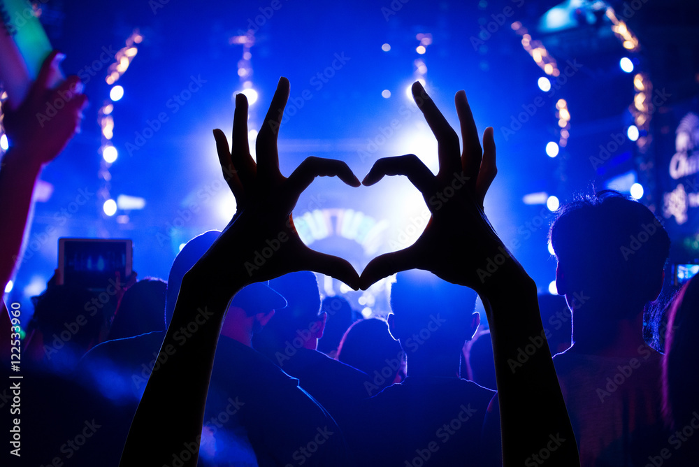 Festival crowd raising hands in music concert front of bright st