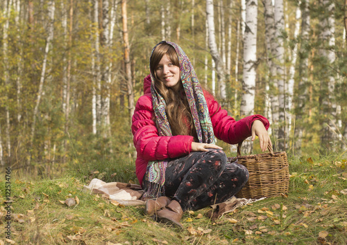 Молодая женщина сидит в лесу с корзиной