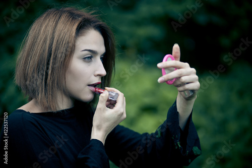 Girl with idela face features adjusts her lipstick while looking photo