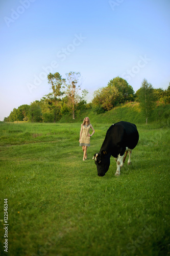 Girl walks to the cow across the green field © IVASHstudio