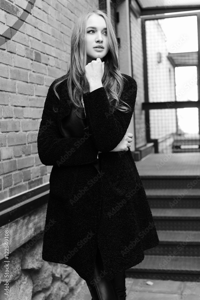 Black and white photo. Beautiful young blonde woman walking on the street. Dressed in a black coat and a warm knit sweater. Black and white photo. Beautiful young blonde woman walking on the street. Dressed in a black coat and a warm knit sweater.